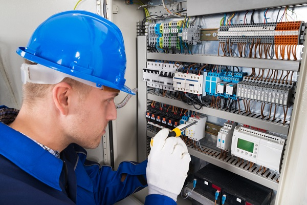 Electrician in a hard hat testing breakers inside an open control panel